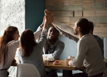 Diverse excited best friends raising hands giving high five together at meeting in cafe, happy multiracial students group promising unity support in good friendly relations hanging in coffee house