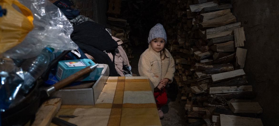 Uma menina de três anos é forçada a se proteger do bombardeio em andamento com sua família em um porão escuro e úmido em Lyman, na Ucrânia