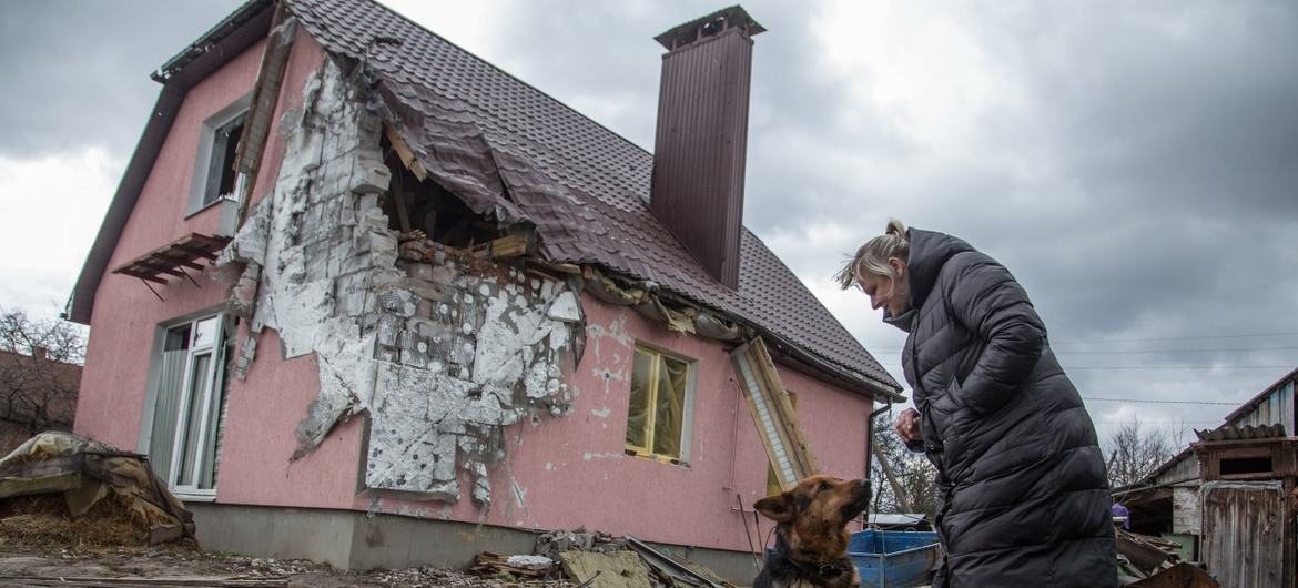 Mulher ucraniana com seu cachorro está no meio de uma casa danificada.