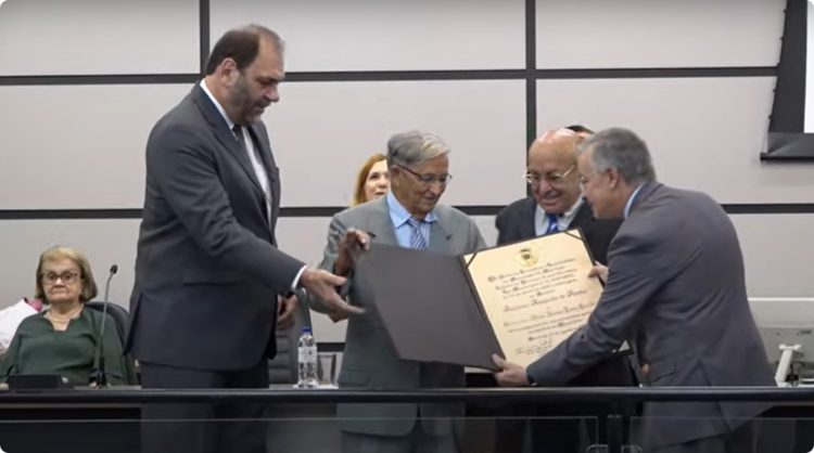 A. A. de Assis recebe a comenda das mãos dos vereadores Mario Verri e Manoel Sobrinho e do secretário Clóvis Melo, representando o prefeito Ulisses Maia Foto: Reprodução